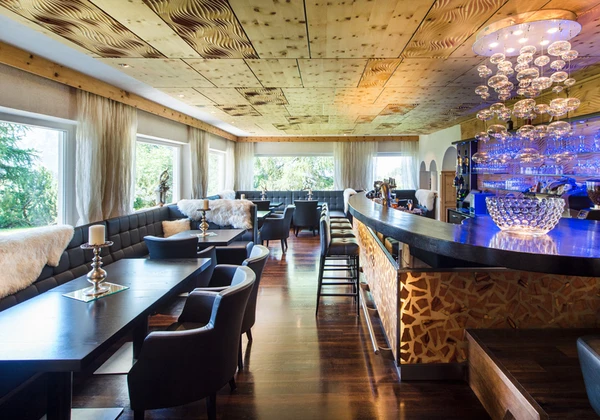 Bar moderno dell'hotel con illuminazione elegante, mobili scuri e comode sedie in un interno dal design elegante con elementi in legno. - Bild größer darstellen