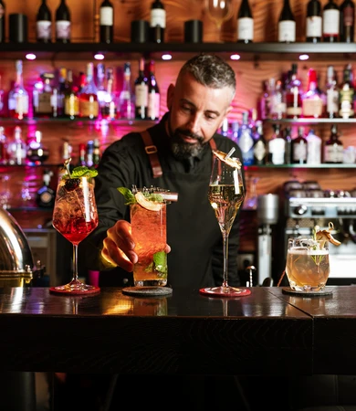 Un barista dell'Hotel Rosa serve cocktail elaborati davanti a un bar con infrastruttura tecnologica Internet e scaffali per bottiglie illuminati. - Bild größer darstellen