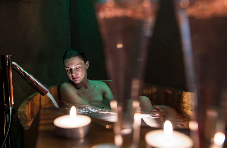 Una donna si rilassa nella vasca idromassaggio in legno dell'Hotel Rosa, avvolta dalla luce delle candele, per una pausa relax nelle Dolomiti vicino all'Alpe di Siusi. - Bild größer darstellen