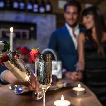 Una coppia gusta romanticamente lo spumante Ferrari con fragole al lume di candela in un ambiente elegante, ideale per un soggiorno all'Hotel Rosa. - Bild größer darstellen