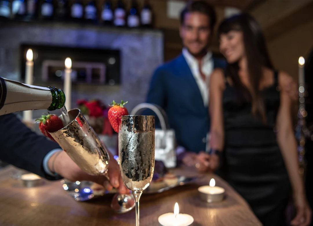 Una coppia gusta romanticamente lo spumante Ferrari con fragole al lume di candela in un ambiente elegante, ideale per un soggiorno all'Hotel Rosa. - Bild größer darstellen