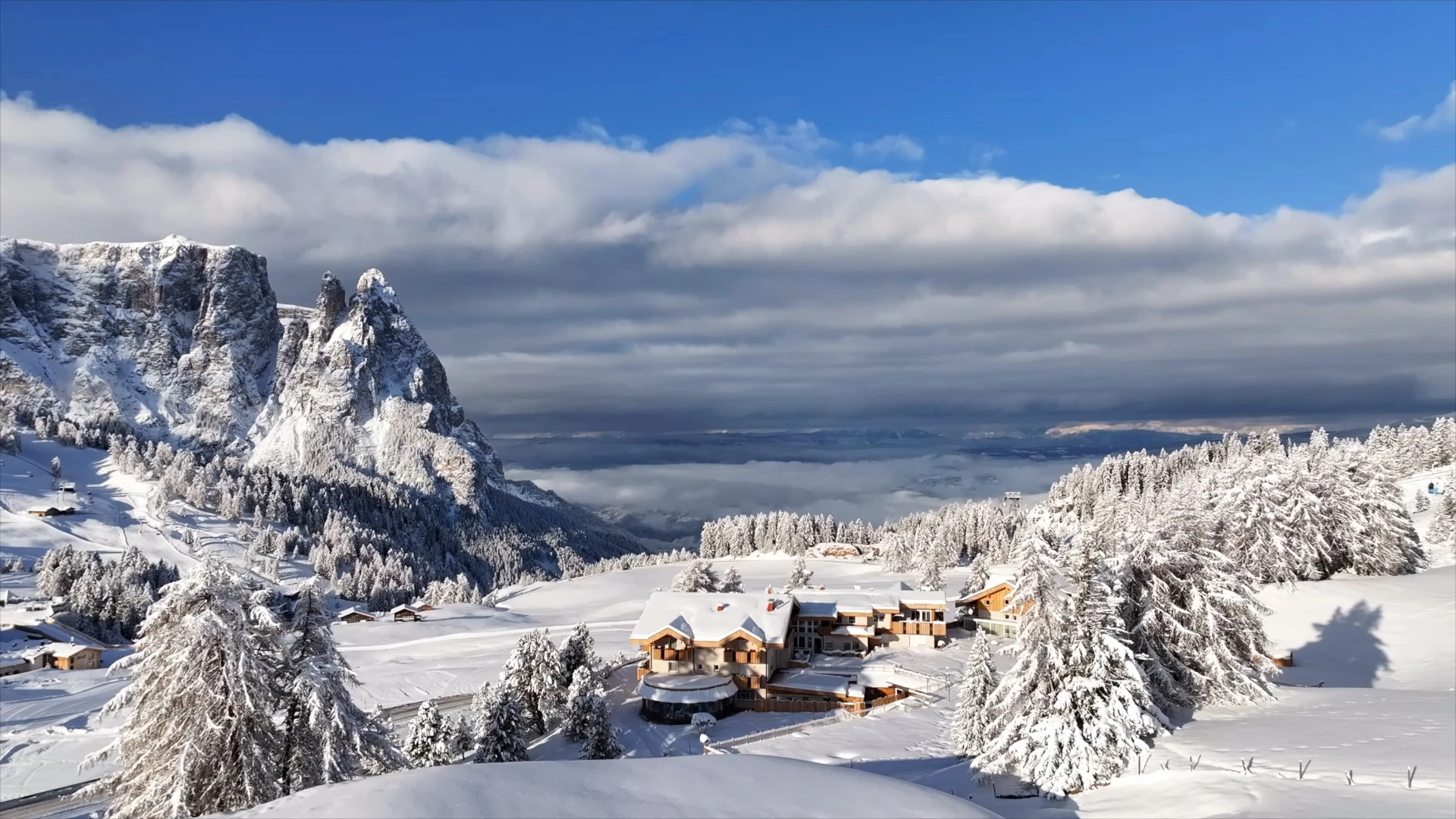 L'edificio di un hotel coperto di neve è immerso in un paesaggio montano invernale sotto un cielo blu profondo con spesse fasce di nuvole.