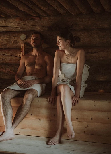 Una coppia si rilassa nella sauna dell'Hotel Rosa nelle Dolomiti vicino all'Alpe di Siusi, circondata da boschi rustici per un'esperienza di benessere esclusiva. - Bild größer darstellen