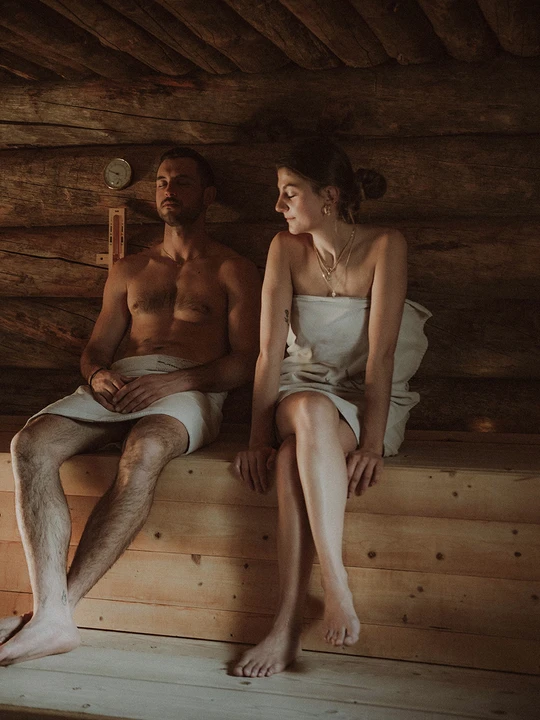 Una coppia si rilassa nella sauna dell'Hotel Rosa nelle Dolomiti vicino all'Alpe di Siusi, circondata da boschi rustici per un'esperienza di benessere esclusiva. - Bild größer darstellen