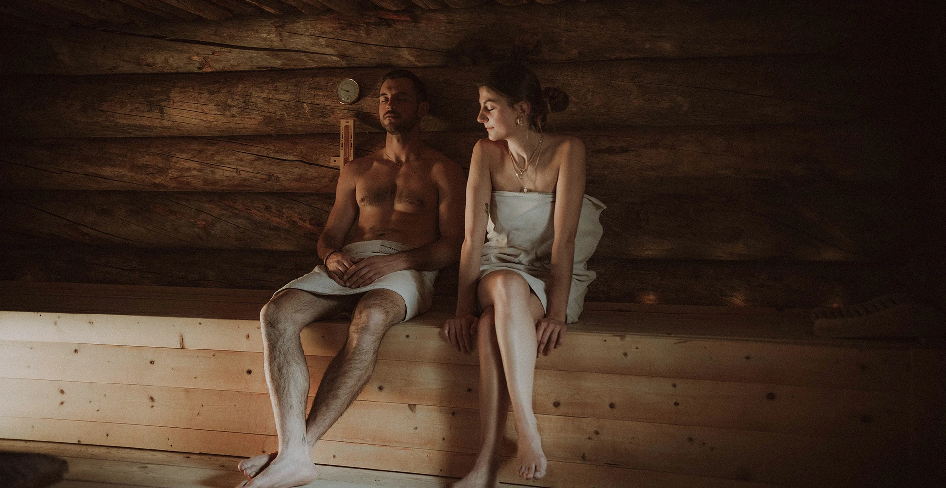 A couple relaxes in a rustic wooden sauna at Hotel Rosa, surrounded by the calming atmosphere of the Dolomites for a relaxing wellness holiday.