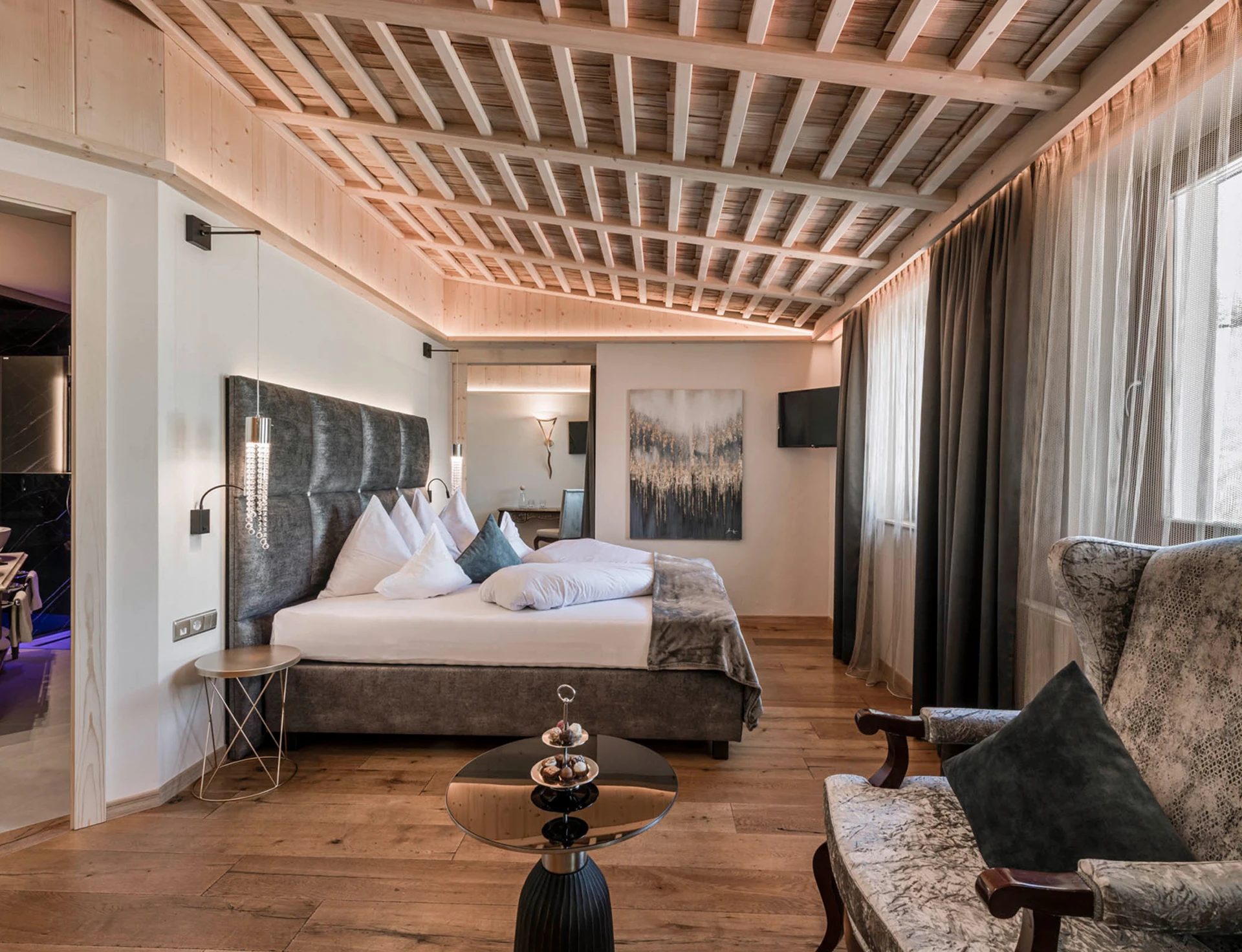 Una lussuosa camera d'albergo con un comodo letto, soffitto con travi in ​​legno, un'elegante poltrona e un bagno annesso con doppio lavabo.