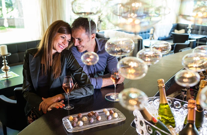 Una coppia felice si gode una serata romantica con spumante e cioccolatini al bar dell'Hotel Rosa vicino all'Alpe di Siusi nelle Dolomiti. - Bild größer darstellen